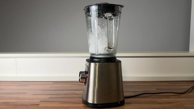 Close up video of an immersion blender crushing ice in a container. Concept of food preparation, cold drinks, smoothies, cocktails, and modern kitchen technology.