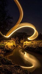 Nighttime light trails above a stream, trees, and rocks under a starry sky