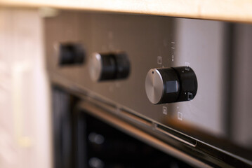 A close-up of the black and silver control knobs of a modern electric oven.