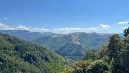 Fototapeta premium Wide panoramic view of green mountain ridges and forests along the Transalpina road in Romania on a clear summer day with blue sky and clouds.