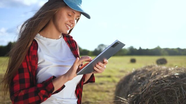 Woman in field holding tablet computer. Girl works on tablet in field. Woman works in a field with haystacks of grass. A woman lifestyle in a field is holding a tablet.