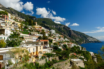 Colorful terraced houses cascade down the steep hillsides of Positano, Italy, overlooking deep blue Mediterranean waters. Lush greenery and dramatic limestone mountains frame the vibrant coastal