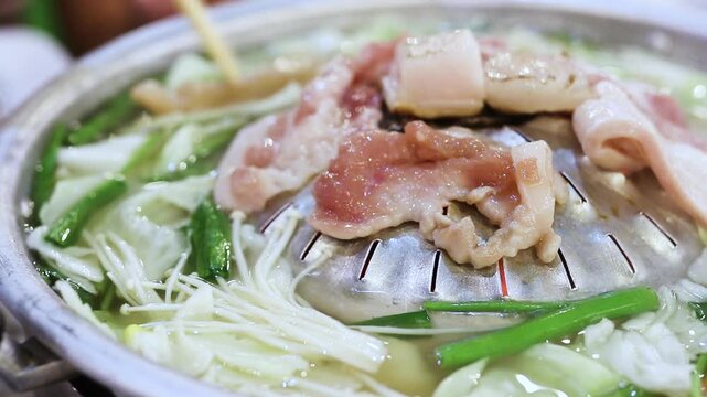 Moo Krata, traditional Thai BBQ, featuring sliced pork belly and vegetables grilling on a dome-shaped pan with hot broth.