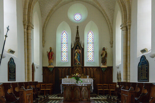 Bright church chancel featuring a central altar, flanked by colorful statues and tall stained glass windows. Ornate woodwork and checkered tile flooring create a harmonious, tranquil atmosphere.