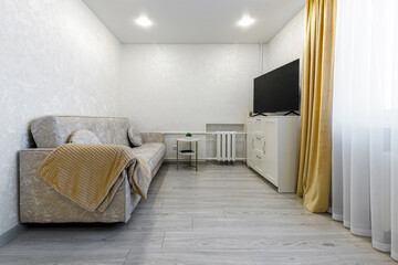 Bright living room interior with beige sofa and TV on white cabinet