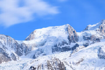 Jagged, snow-covered cliffs and glacial formations dominate Mont Blanc du Tacul, highlighted by soft daylight and wispy clouds drifting across a vivid blue sky.