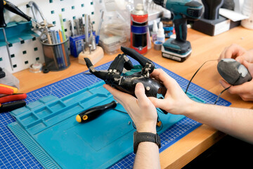 Person holds an advanced black prosthetic hand. The scene takes place on a workbench, with tools, and a blue mat in the background