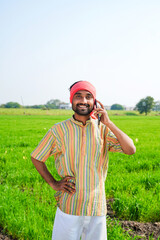 young indian farmer talking on smartphone at agriculture field