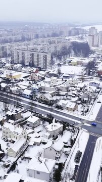 Vertical drone shot of the Dārzciems neighborhood in Riga, Latvia, showcasing the contrast between private villas and high-rise housing blocks during a Baltic snowstorm.
