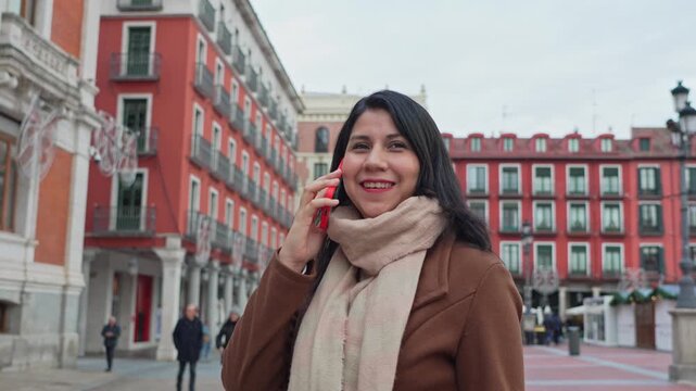 Happy latina woman talking on smartphone in plaza mayor