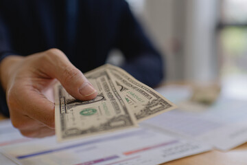 Hand giving US dollar cash to pay monthly bills on desk. Concept of bill payment, personal finance, expense management, household budgeting, debt control and responsible money management.