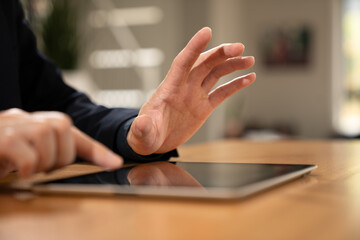 Close-up of a hand interacting with a digital tablet on a wooden desk, representing technology, touchscreen interaction, online work, and digital lifestyle. © Teelapon