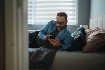 Man relaxing in bed using smart phone for digital connection