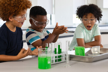 African American school-age boys wearing goggles watching chemistry demo at lab with test tubes