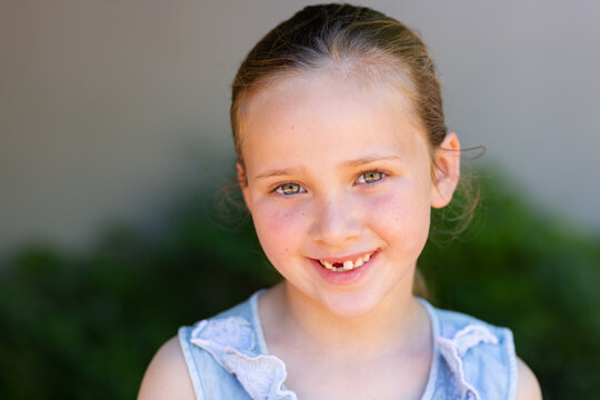 Smiling child girl wearing light blue sleeveless top with lace trim with hair tie in garden