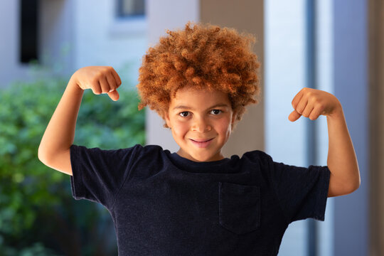 African American school-age boy flexing both arms on porch near column wearing navy tee with pocket