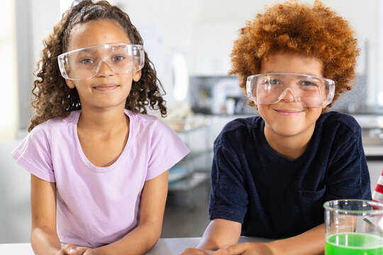 African American children wearing safety goggles seated at school lab examining bright green beaker