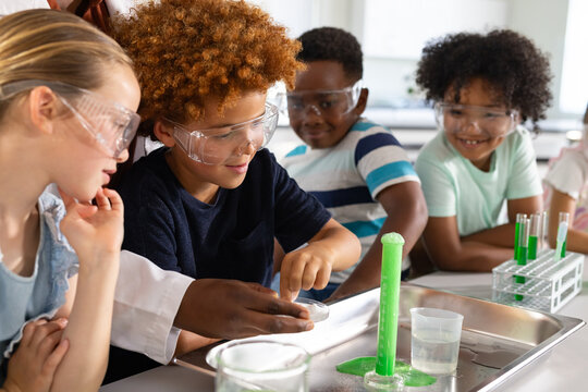 Diverse goggled students lab-coated woman teaching at lab watching green foam rising from cylinder