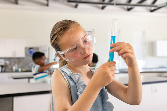Teenage girl wearing light-blue top and goggles examining test tube with blue liquid in school lab