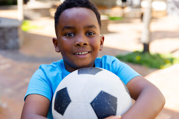 School-age African American boy wearing blue tee holding black white soccer ball smiling at park