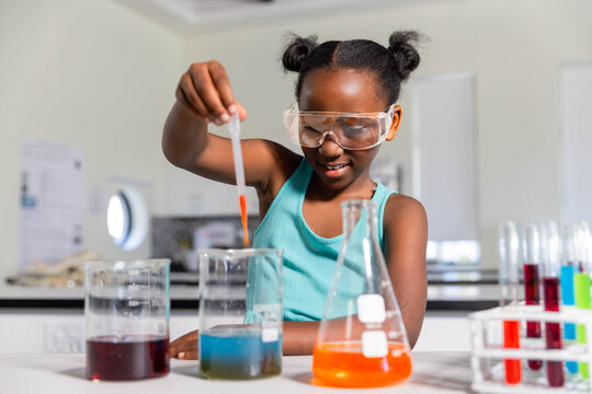 African youth female wearing teal top and goggles holding dropper over beakers in school lab