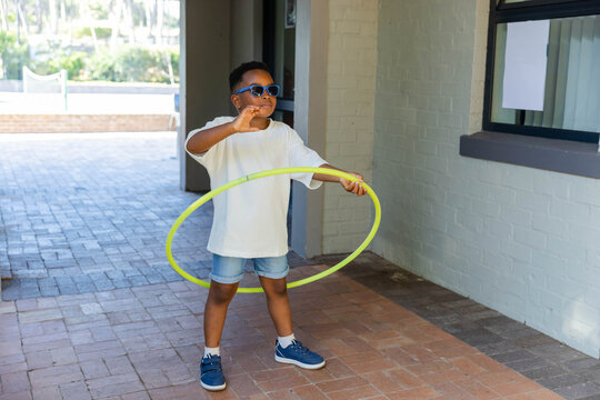 African American child wearing sunglasses and holding neon yellow-green hula hoop on shaded walkway