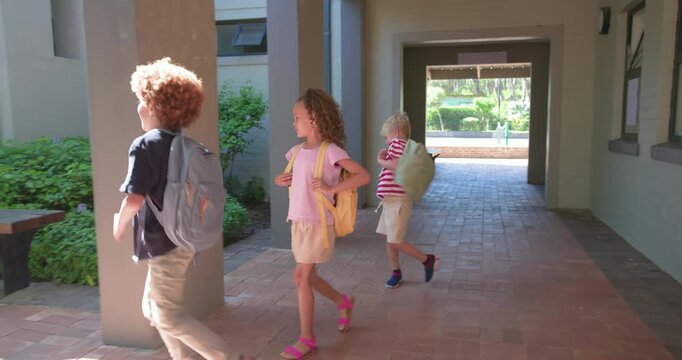 Three schoolkids passing brick arch into sunny courtyard, sorting backpacks on bench getting books