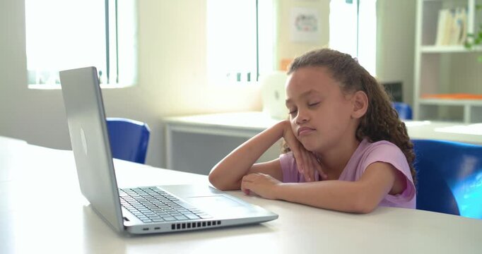 African girl child in purple shirt sitting at school facing laptop, camera moving, appearing bored