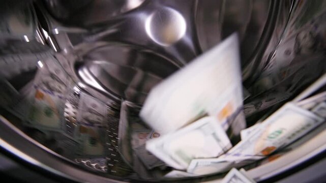 US paper currency spinning around inside a domestic washing machine drum. Money laundering concept.