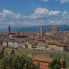 Obraz premium The Arno River winds through Florence, with the grand silhouette of Santa Maria del Fiore Cathedral and the Tower of the Old Palace standing prominently in the city’s historic skyline.