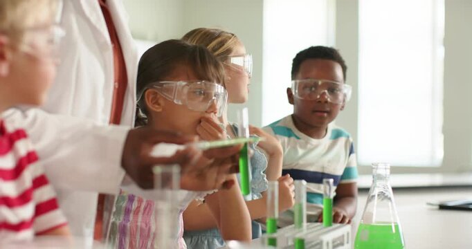 Children watching African American woman teacher showing green test tube at lab bench, observing