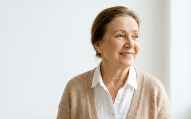 Content senior woman with a warm smile looks thoughtfully to the side, portrait against a bright white background, symbolizing graceful aging and well-being.