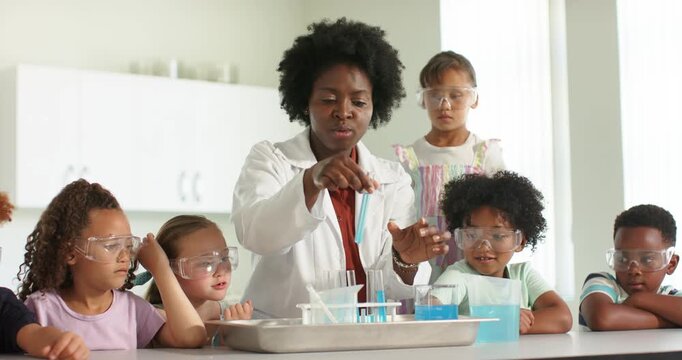 African American teacher holding blue pipet pouring into rack teaching students with goggles in lab