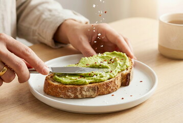 Hands preparing a delicious avocado toast on sourdough bread, topped with sea salt and chili flakes. A healthy and fresh breakfast meal.