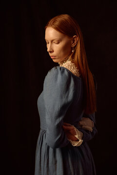 Caucasian young adult woman standing with eyes closed and head turned to side, long straight red hair visible, wearing vintage style dress, hands clasped behind back