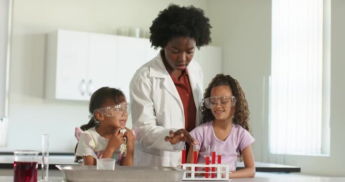 Instructor in lab coat lifting red test tube guiding goggled youth dipping into cup for lab