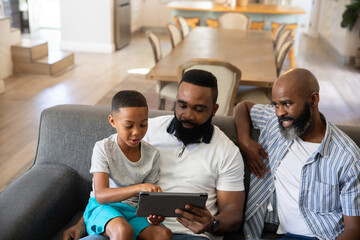 African American family sitting on gray fabric couch in living room engaging with tablet device