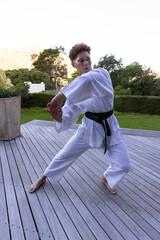 African american woman practicing karate on deck near planter wearing white gi and black belt