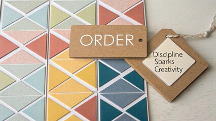A kraft paper tag with the word ORDER displayed prominently over a vibrant, diagonally aligned geometric color card pattern