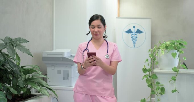 Adult female nurse wearing stethoscope reading message on red phone, smiling, laughing at reception