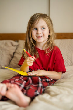 Smiling child writing Christmas greeting card at home in pajamas