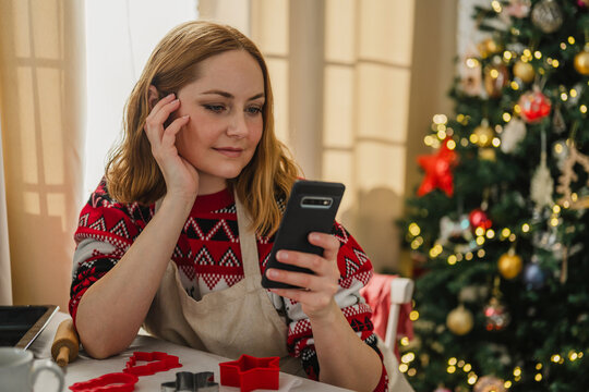 Woman baking gingerbread cookies using recipe on smartphone at Christmas