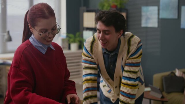 Tilt up shot of cheerful young man greeting female newcomer unpacking stuff at modern office workplace
