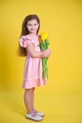 Cheerful happy girl with tulips flower bouquet in pink dress on yellow background