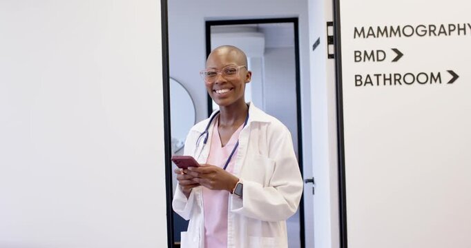 African American woman in lab coat reading phone message, smiling, laughing in clinic door, signage