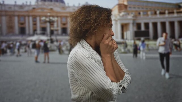 Woman holds arms across chest, hands clasped to collarbone while standing in vatican building square; anxiety vulnerability.