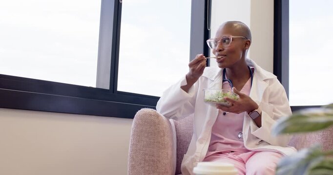 Medical professional is eating salad and sitting in pink chair on break beside window