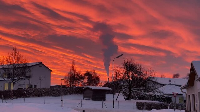 Winter morning scene shortly before sunrise with dramatic orange clouds and smoke rising from a power plant in Lembach im M&uuml;hlkreis, Austria. Quiet village landscape with snow and industrial atmospher