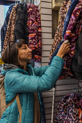 Fototapeta premium A girl examines and purchases clothes at a street market in Israel. A girl chooses a warm sweater in a store.