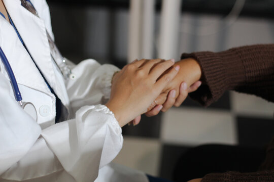 Senior patient lying in hospital bed receiving comforting touch from young female nurse, hands gently clasped together, medical care setting visible